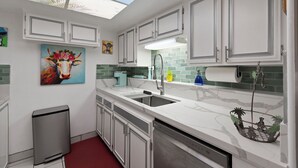 Una cucina moderna con mobili bianchi, un lucernario, un quadro e un portavaso decorativo.