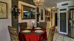 Zona pranzo con tovaglia rossa, sedie in vimini, un lampadario e un grande specchio a parete.