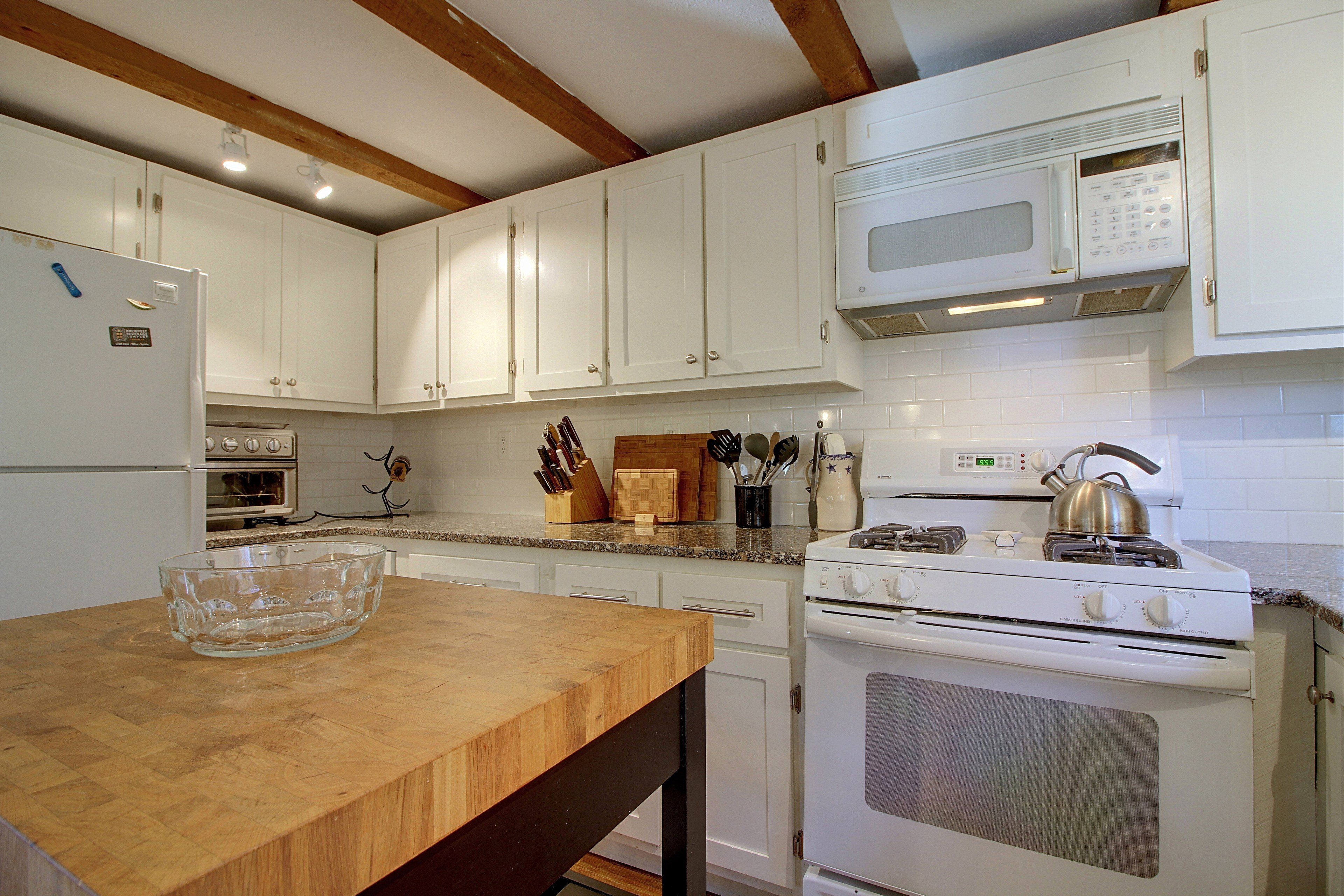 A kitchen with white cabinets, a microwave, an oven, and a wooden table with a glass bowl.
