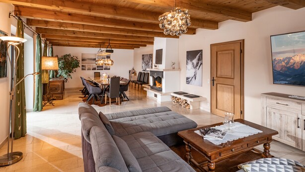 A spacious living area with a high ceiling, a fireplace, a dining table, and a large sofa. - Exclusive Villa Tirol (Fieberbrunn)