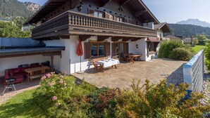 A two-story chalet with a balcony, a patio with outdoor furniture, and a view of mountains. - Exclusive Villa Tirol (Fieberbrunn)