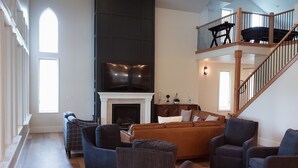 Een ruime woonkamer met een open haard, een trap en een balkon.