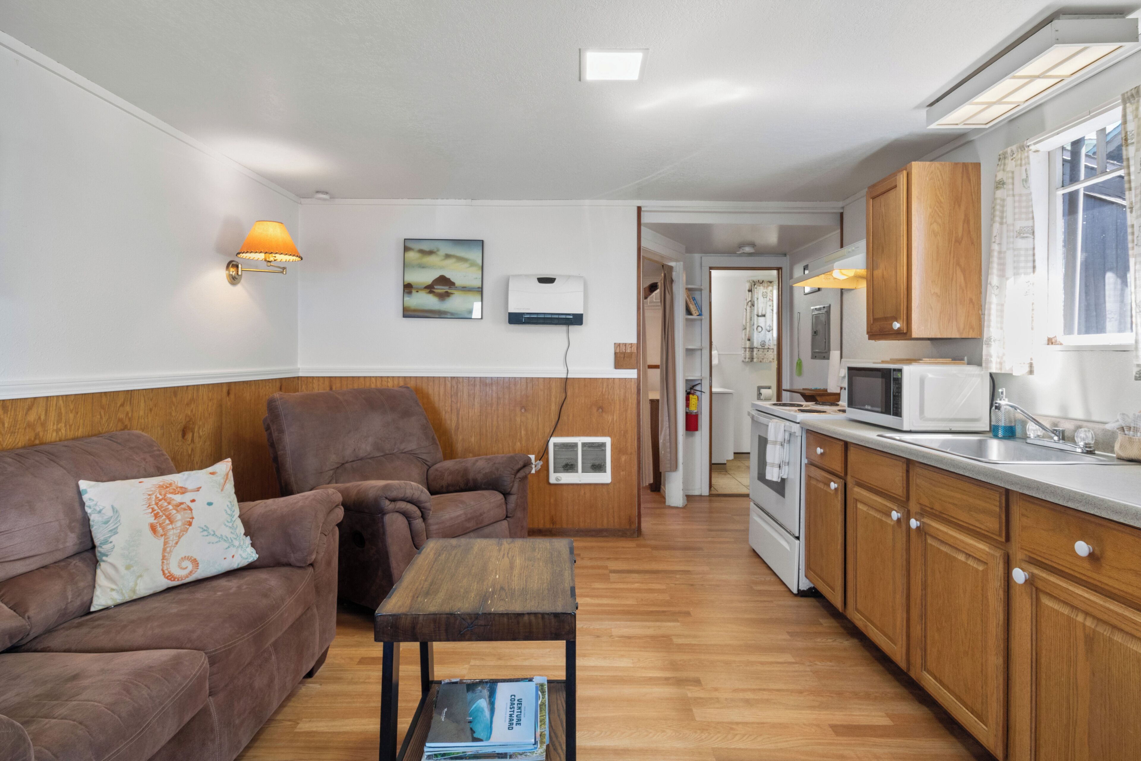 A compact living space with a sofa, a small table, a kitchen area with a microwave, and wooden cabinets.