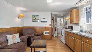A compact living space with a sofa, a small table, a kitchen area with a microwave, and wooden cabinets.