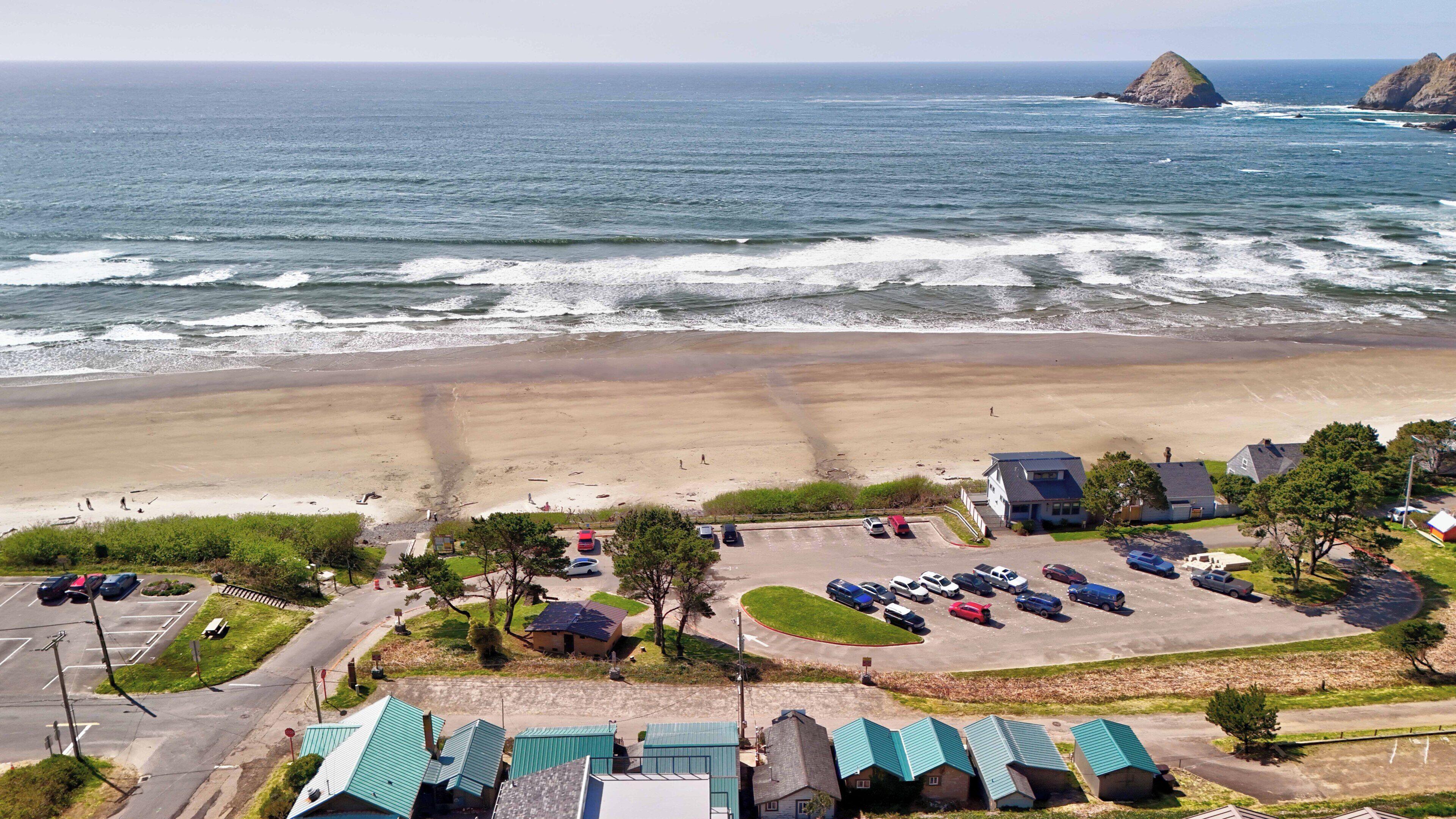 A coastal area with a beach, parking lot, and buildings with green roofs.