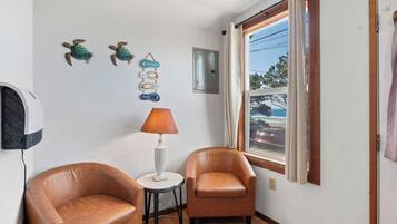 A room with two leather chairs, a small table with a lamp, decorative wall art, a window with curtains, and a wall-mounted air conditioner.