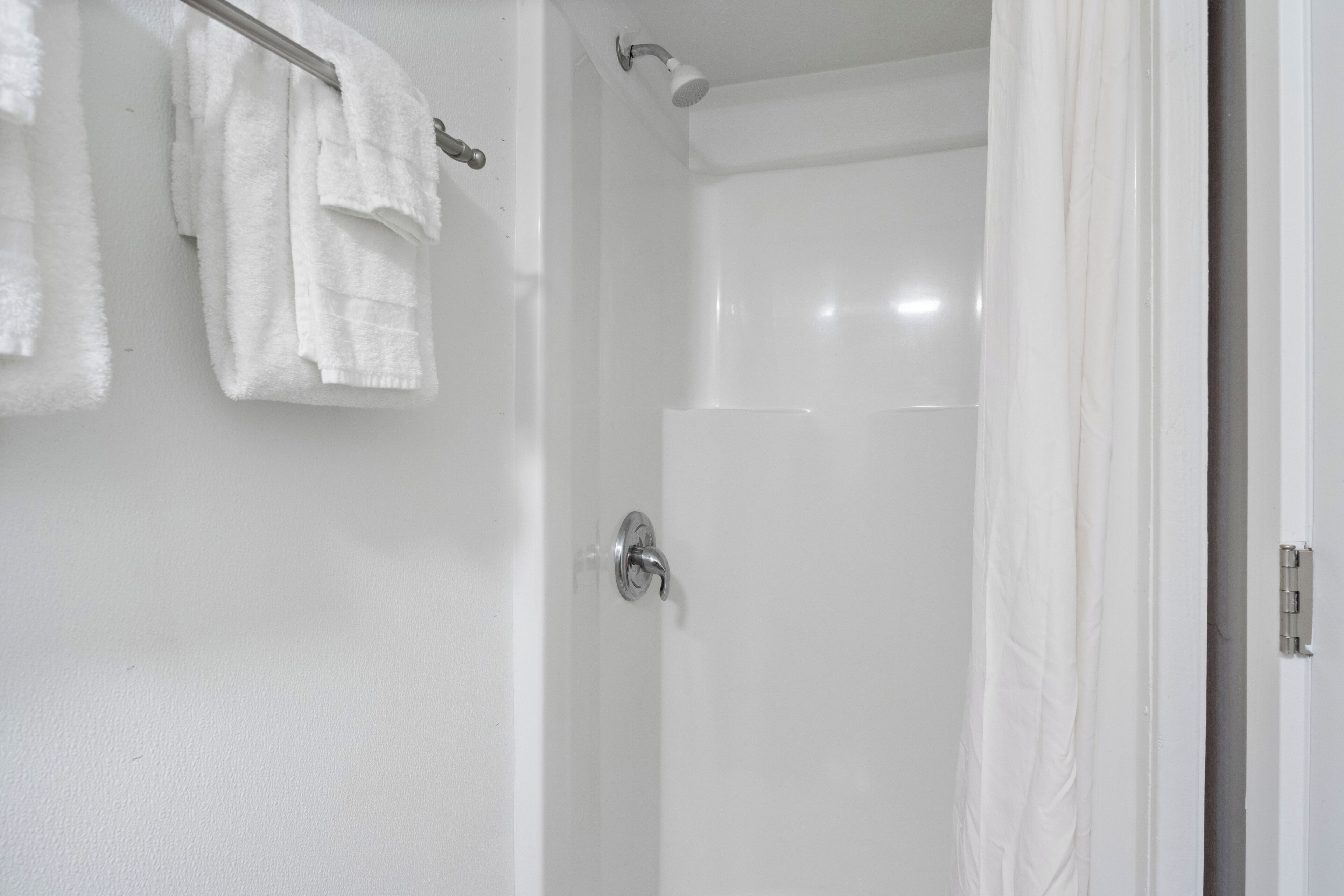 A bathroom with a shower, a towel rack with white towels, and a door with a silver handle.