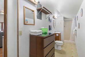 A bathroom with a wooden vanity, a toilet, a shower, and a mirror. - Oceanside Ocean Front Cabins (Tillamook)