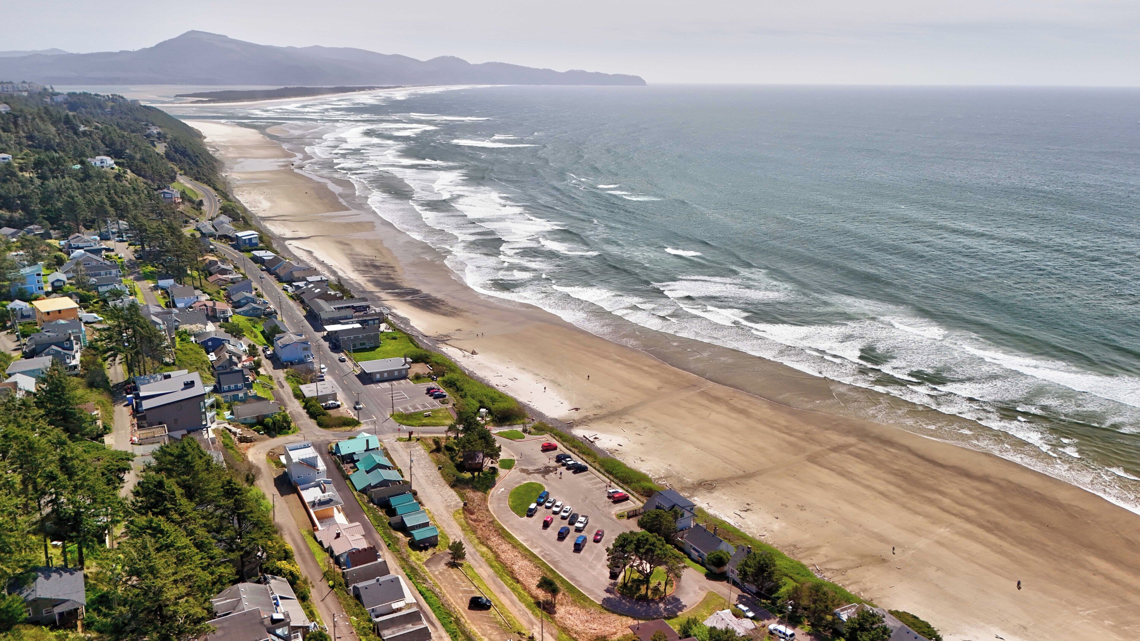 Vista aerea di una zona residenziale costiera con case, una spiaggia e una strada.
