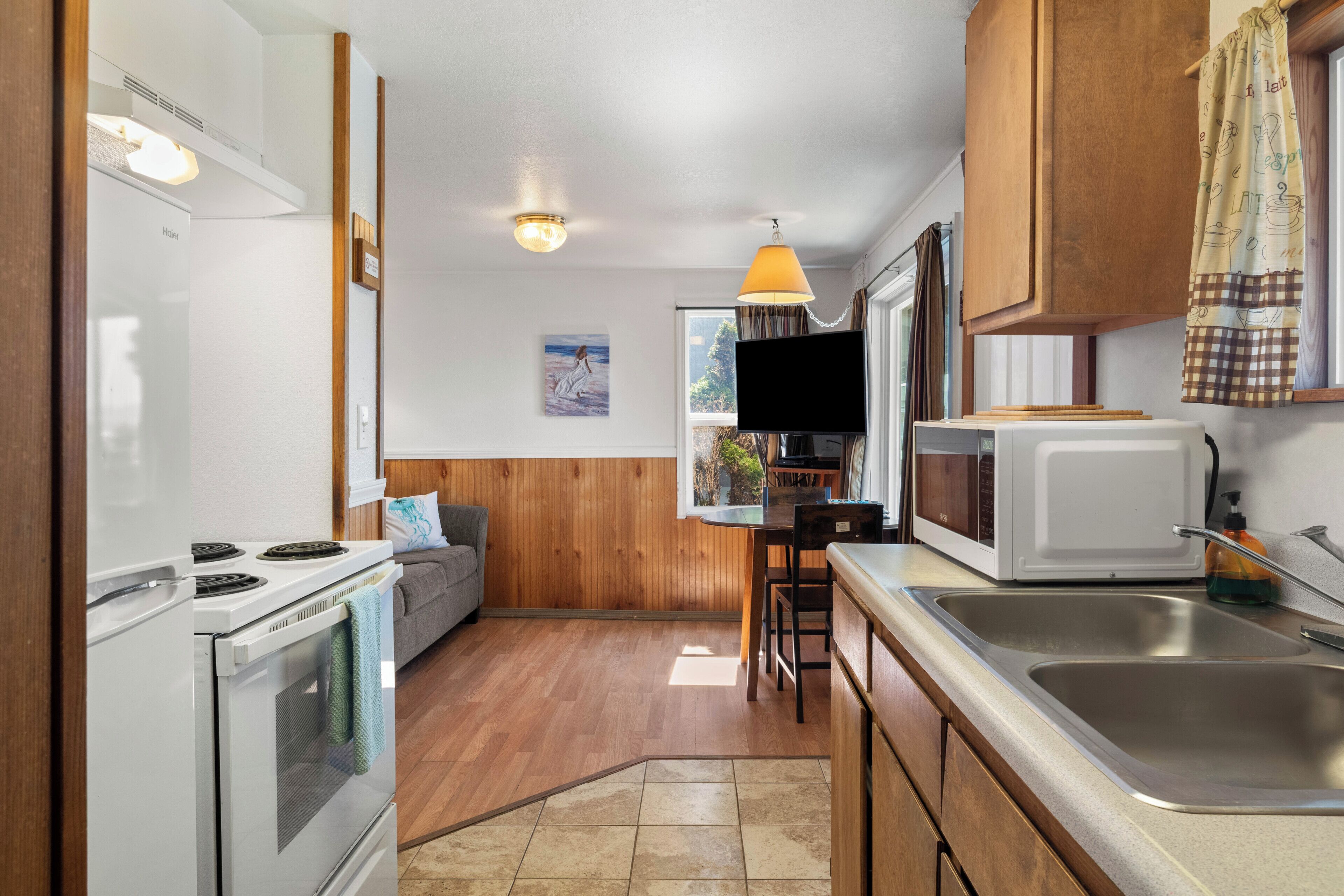 A compact kitchen with a stove, microwave, and sink, wooden cabinets, and a dining area with a table and chairs.