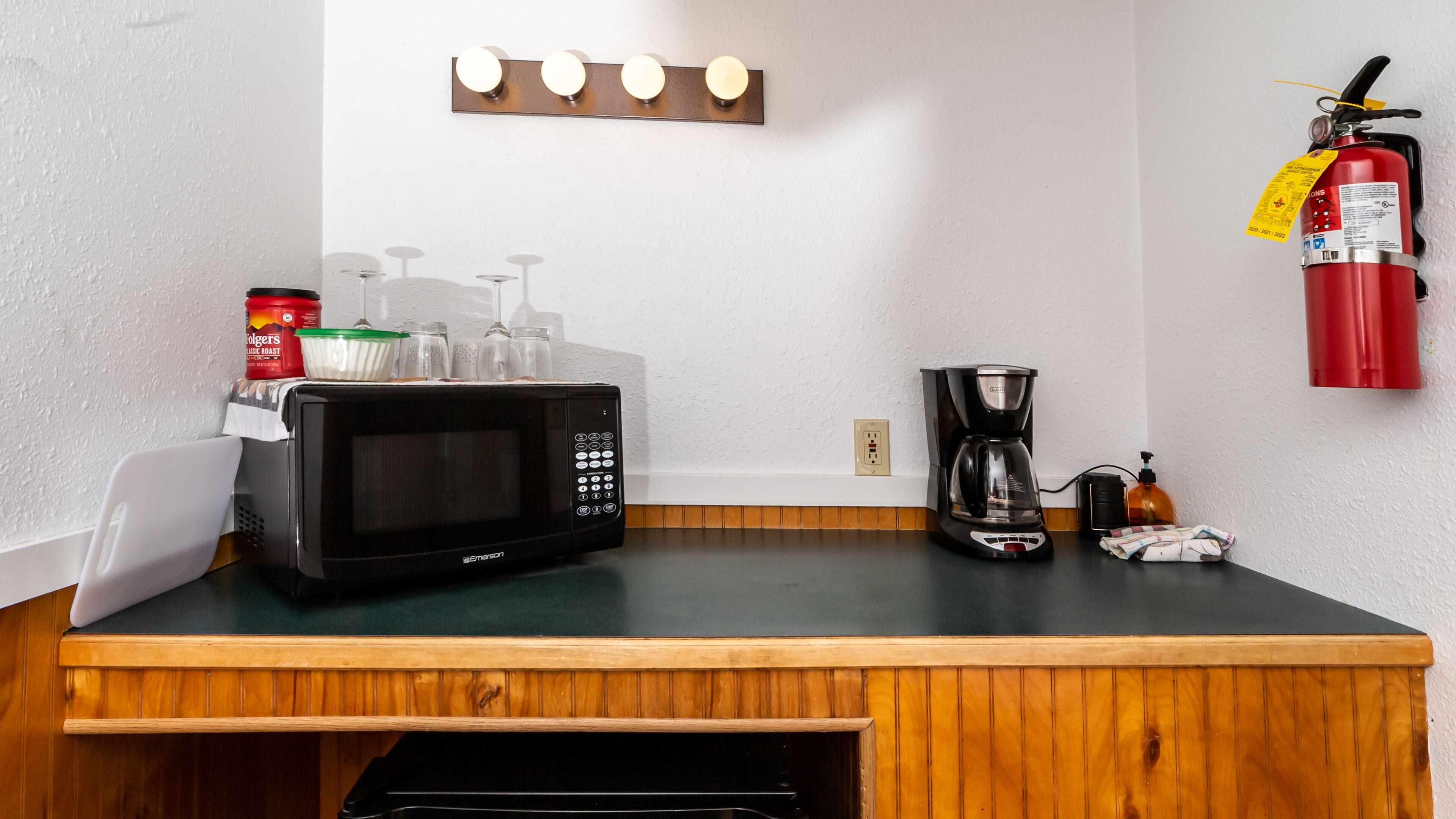 A kitchenette with a microwave, coffee maker, and a fire extinguisher on the wall.