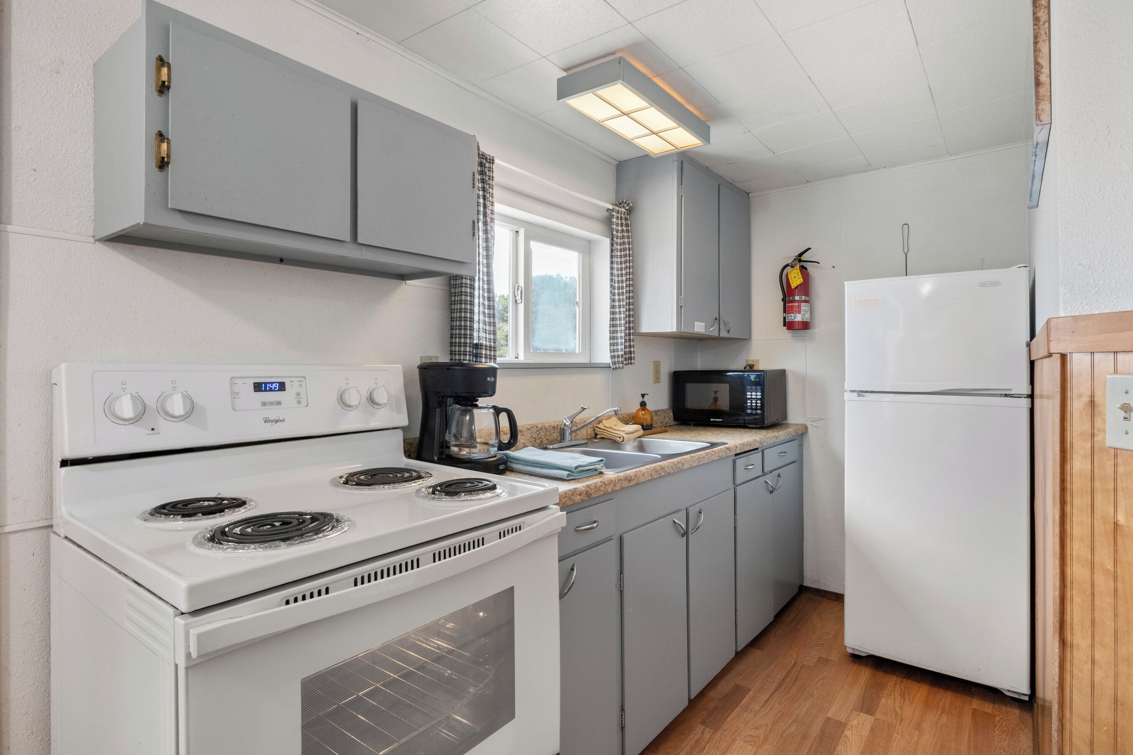 Una cocina equipada con estufa, microondas, refrigerador y una ventana con cortinas.