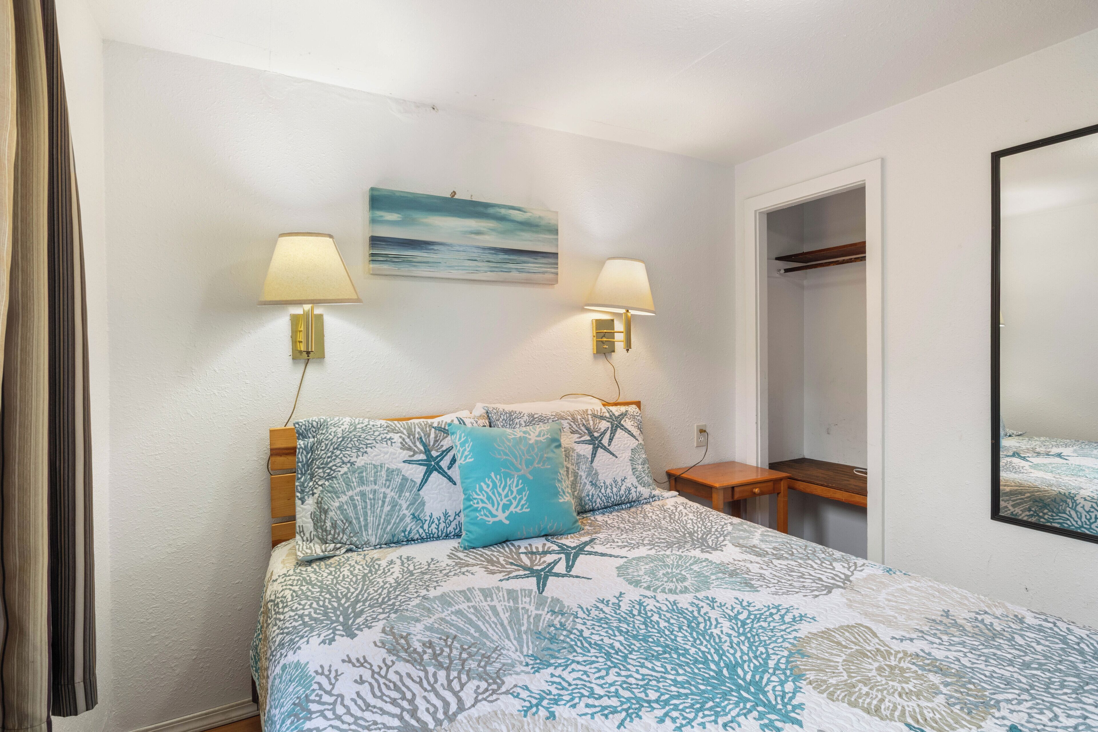 A bedroom with a bed, two wall-mounted lamps, a painting, a wooden nightstand, and a closet.