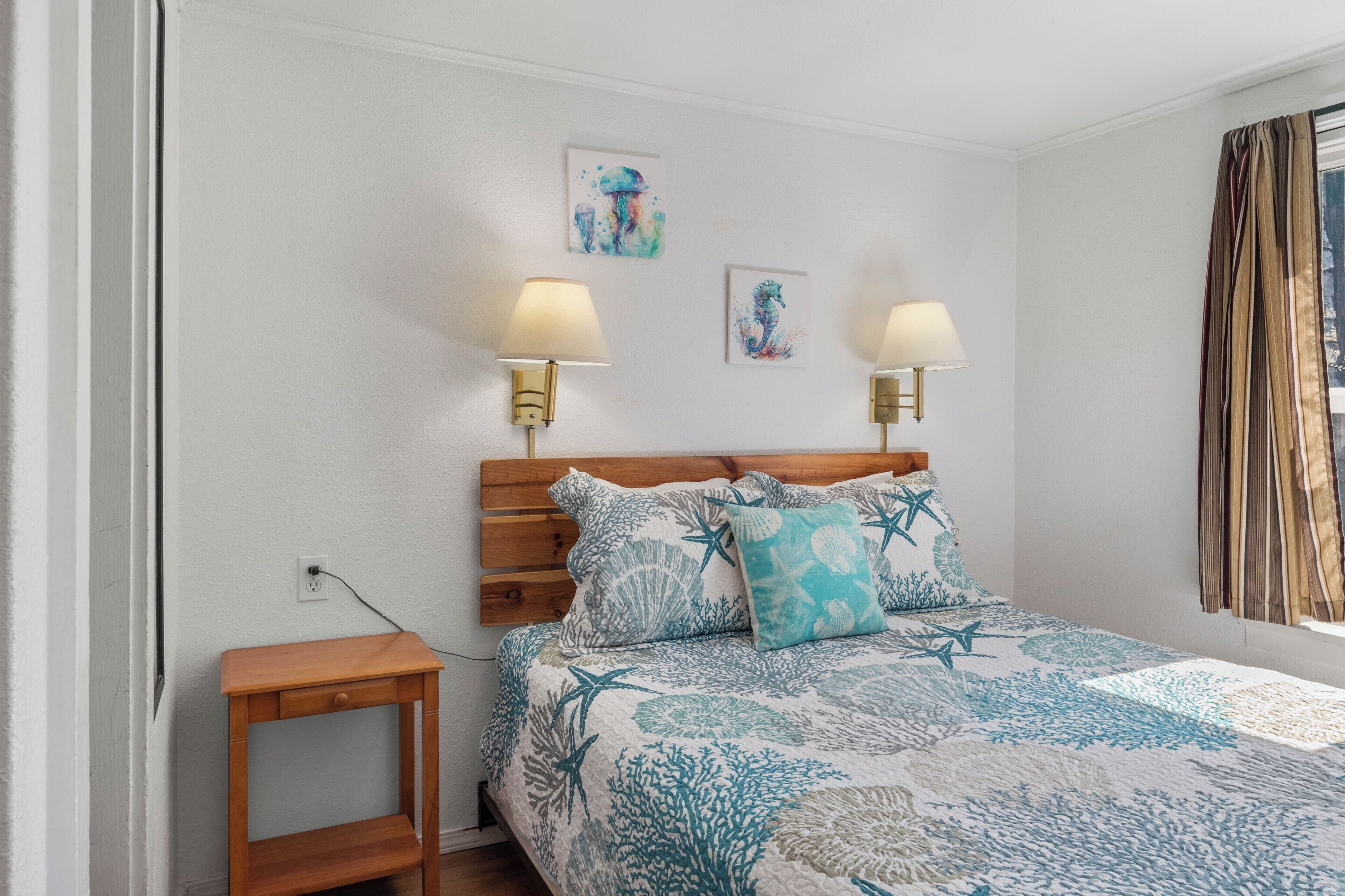 Un dormitorio con una cama, dos lámparas de pared, una mesita de noche y dos obras de arte decorando las paredes.