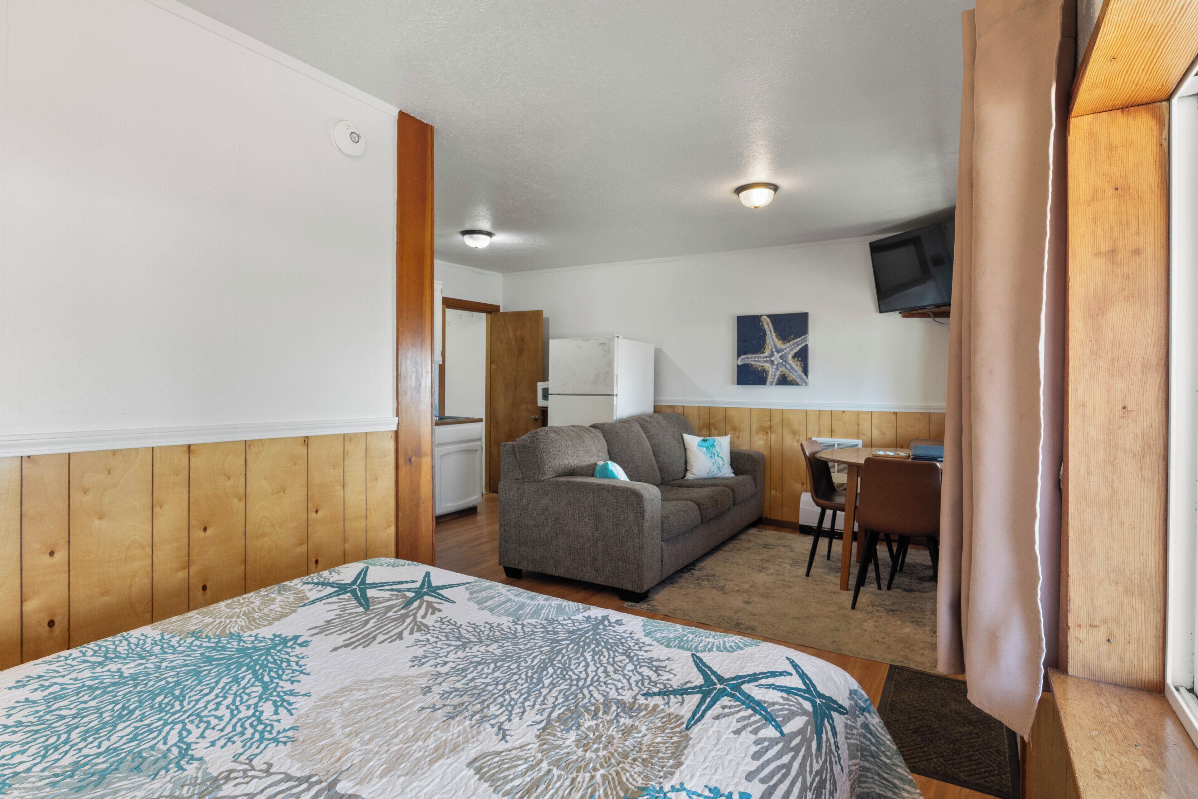 A room with a bed, a sofa, a dining area, a television, and a refrigerator.