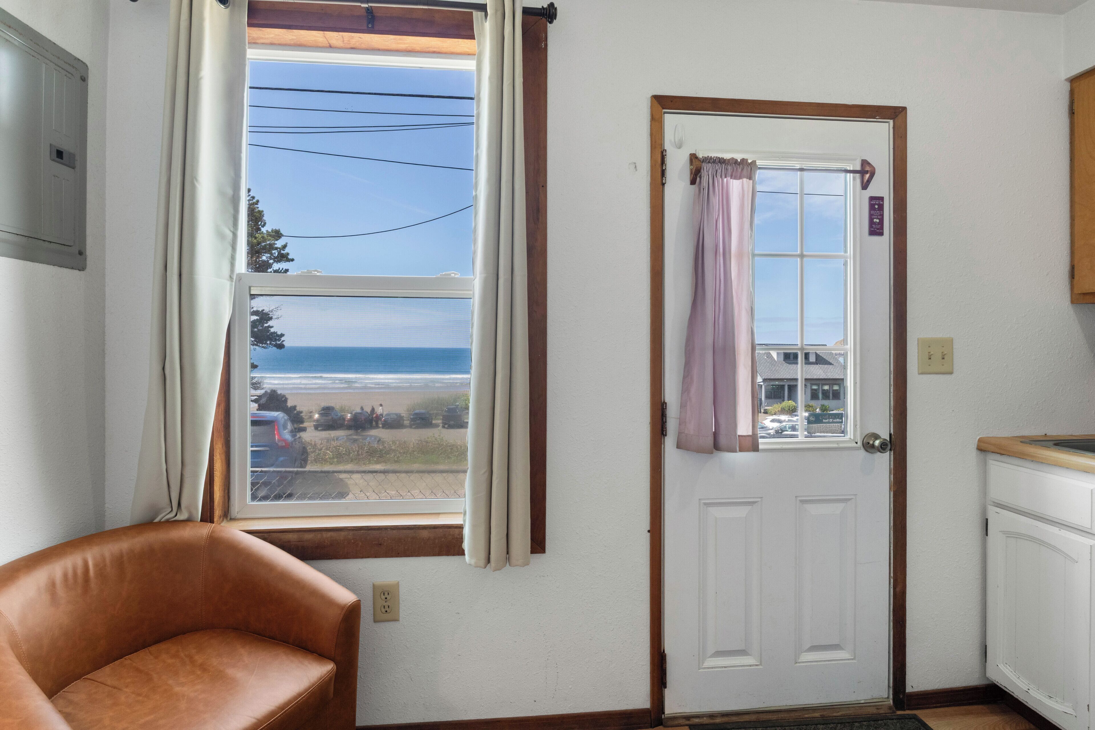A room with a view of the sea, a door with a curtain, a brown leather chair, and white cabinets.