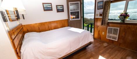 Un dormitorio con cama de madera, ventana con vista al mar y puerta que da al exterior.