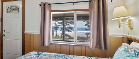 A bedroom with a bed, a window with curtains, a door, and a wall-mounted lamp.