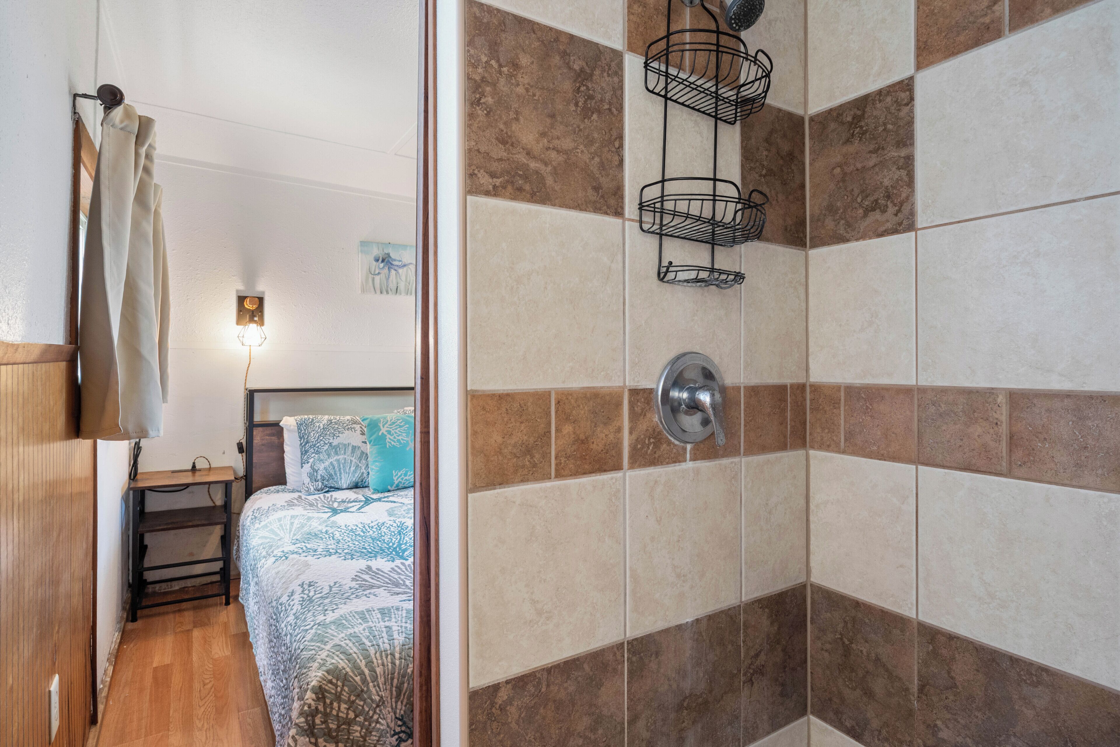 Un baño con ducha, paredes de azulejos, un perchero y una cama con colcha estampada.