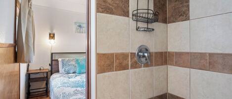 Un baño con ducha, paredes de azulejos, un perchero y una cama con colcha estampada.