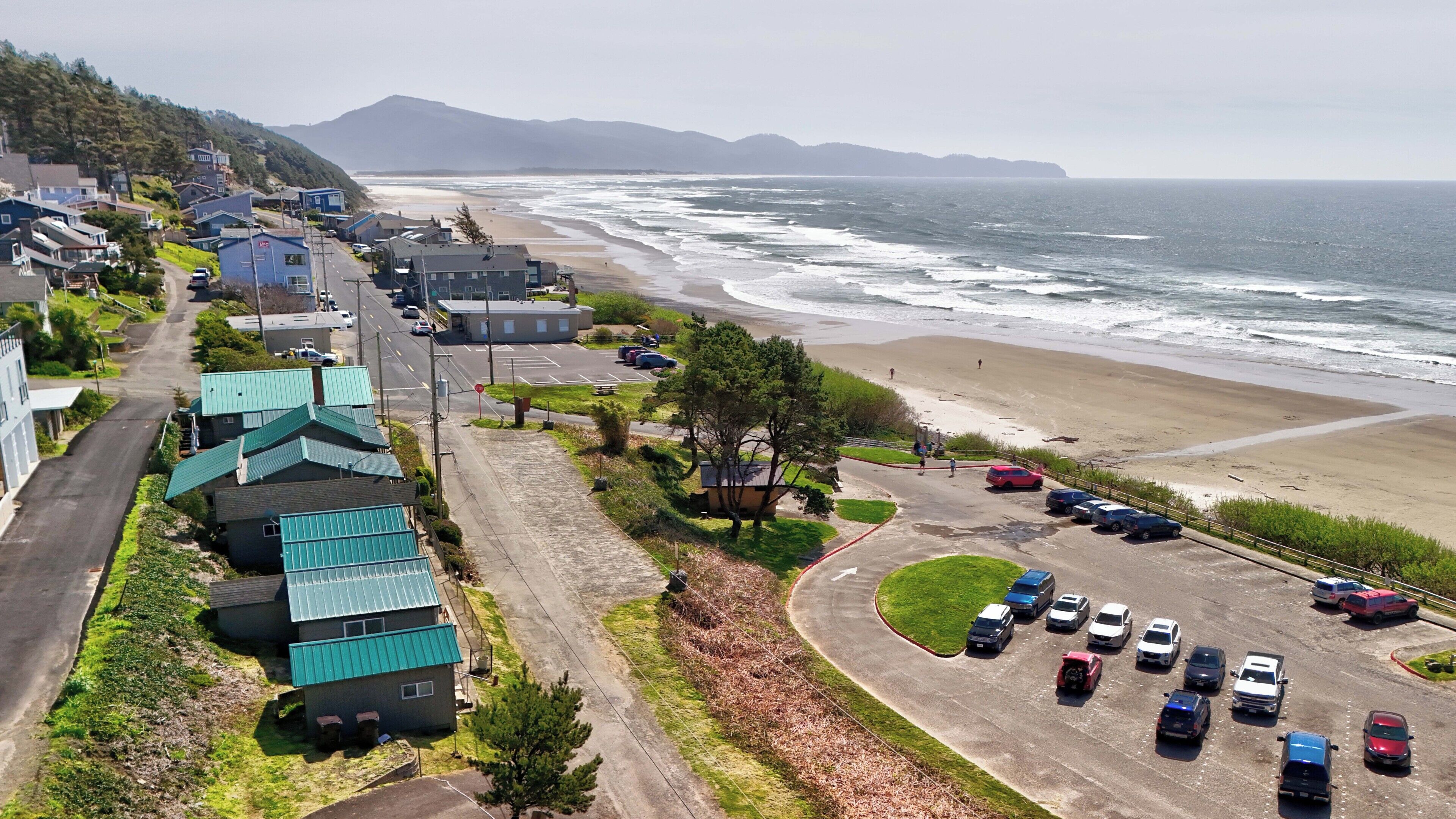 A coastal road with parked cars, a beach, and residential buildings.
