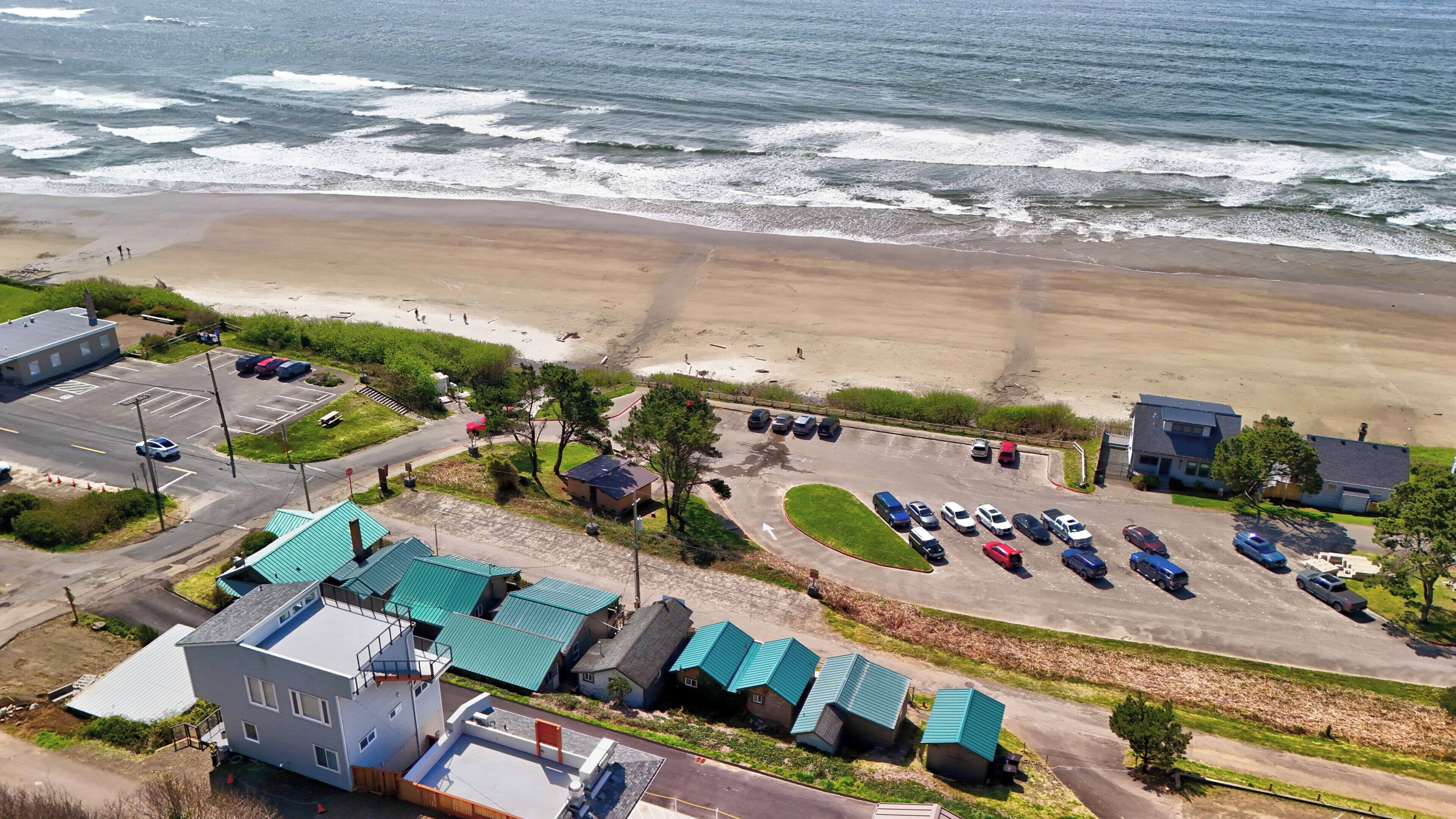 An aerial view of a coastal area with a beach, parking lot, and buildings with green roofs.