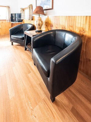A room with a black leather sofa, a wooden table with a lamp, and a television on a wooden stand.