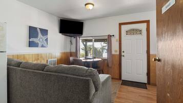 Una habitación con sofá, televisor, una puerta con un letrero y una ventana con cortinas.