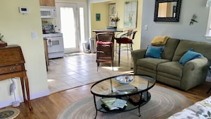 Un salon avec une table basse en verre, un canapé avec des coussins bleus et un coin repas comprenant des chaises et une table.