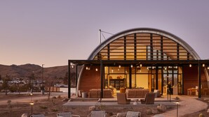 Un bâtiment moderne doté d’un toit incurvé et de grandes fenêtres, entouré d’un espace extérieur aménagé avec des sièges et un foyer.