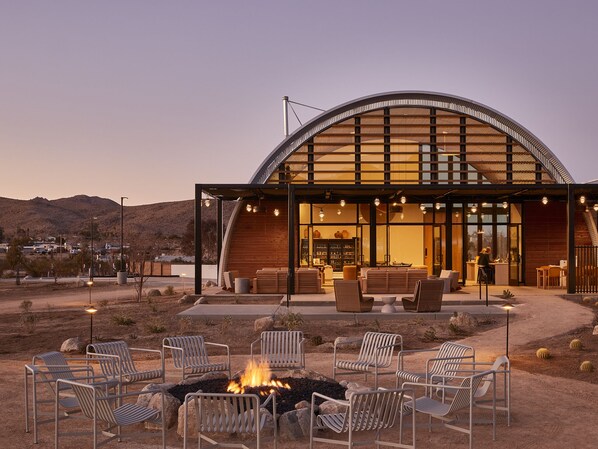 A modern building with a curved roof and large windows, surrounded by outdoor seating and a fire pit.
