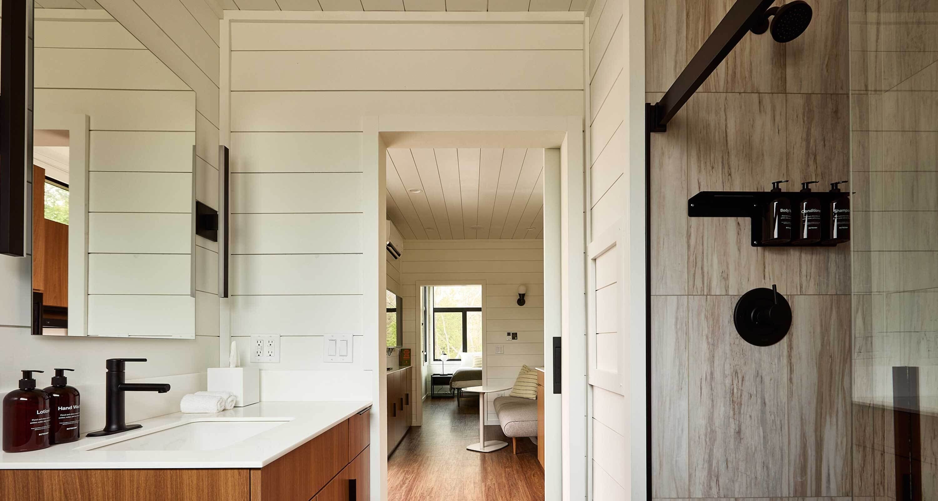 A modern bathroom with a large mirror, a black faucet, and a shower area with a wooden wall.