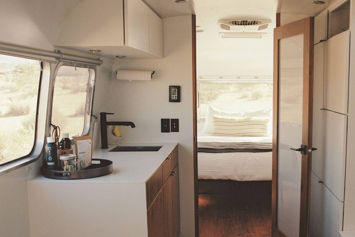 A compact RV interior with a kitchenette, a bed, and a small bathroom.
