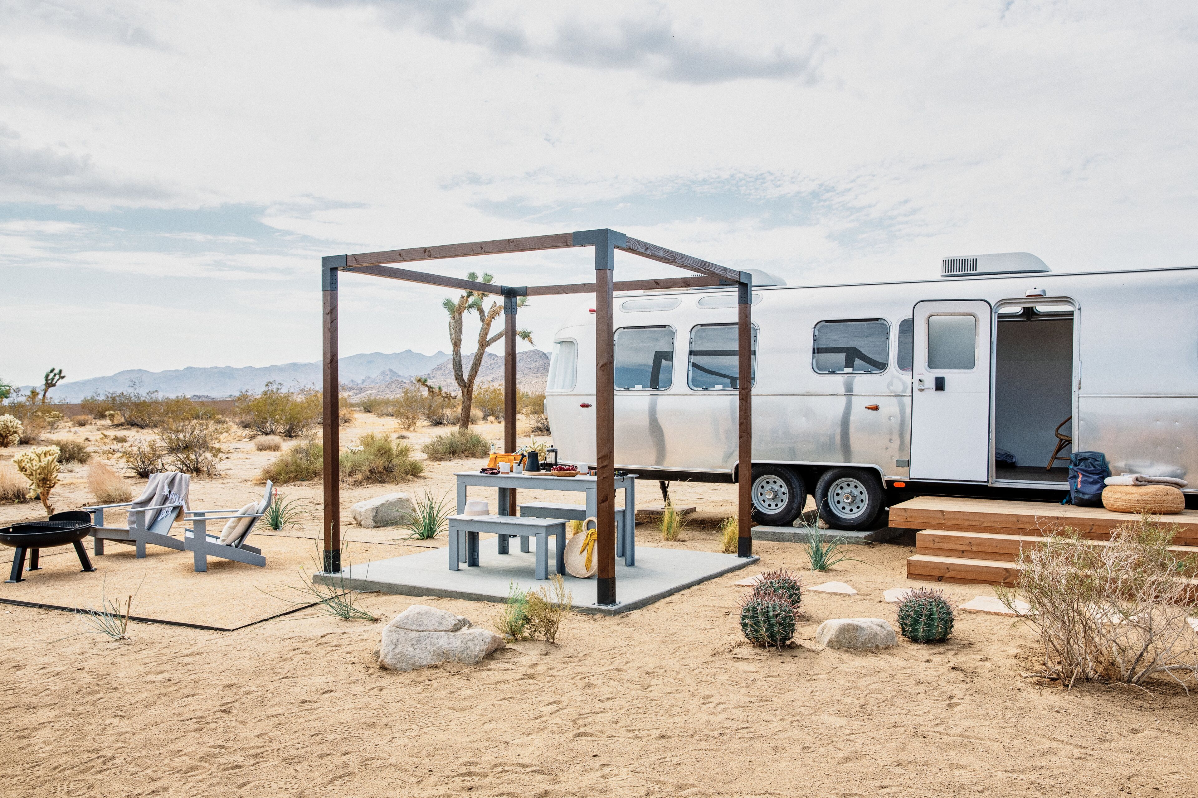 Acampamento no deserto com uma estrutura de metal, uma mesa de jantar e uma RV branca.