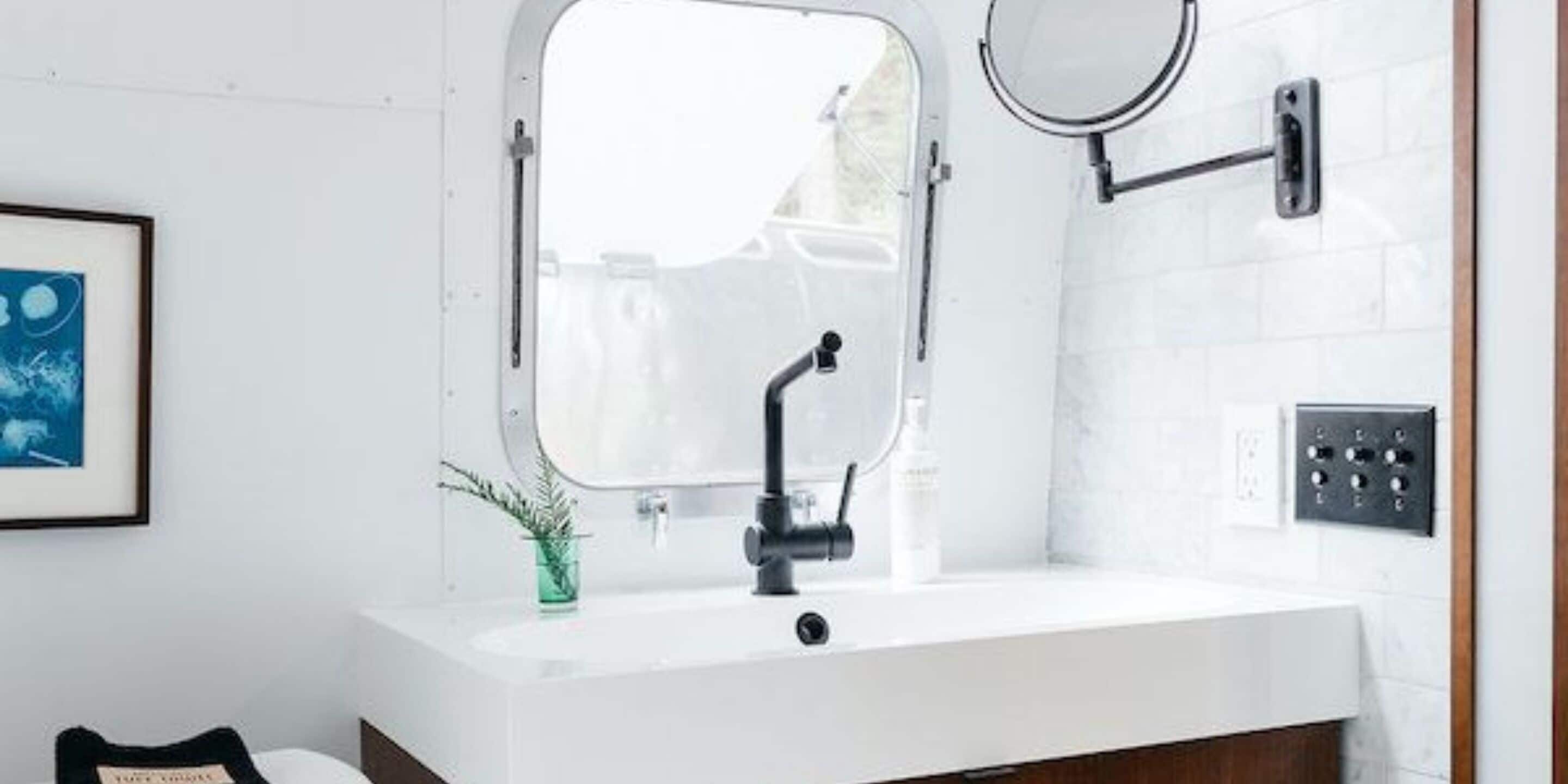 A modern bathroom with a white sink, a mirror, and a window.