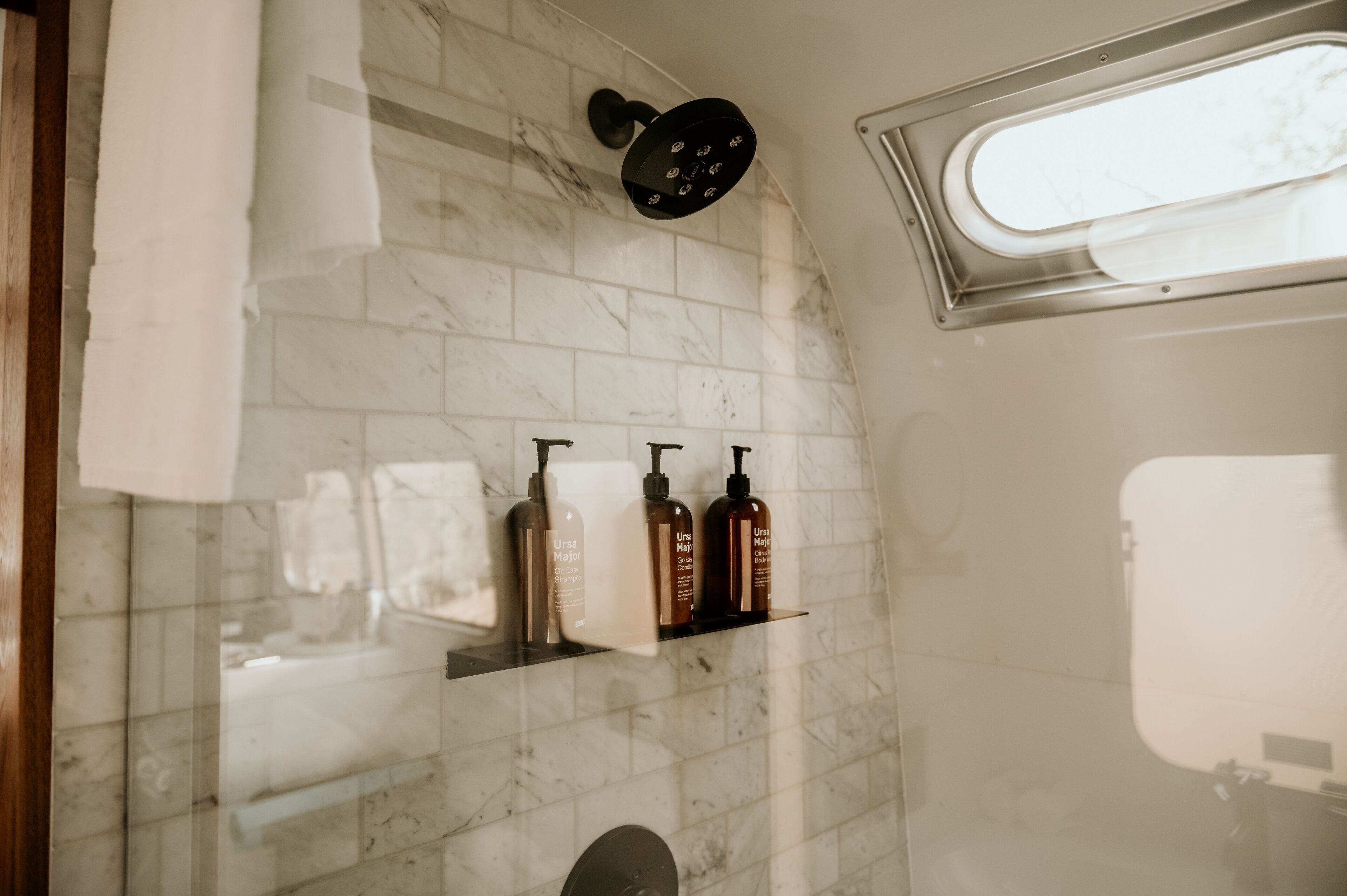 A bathroom with a marble floor, a showerhead, and a shelf with toiletries.