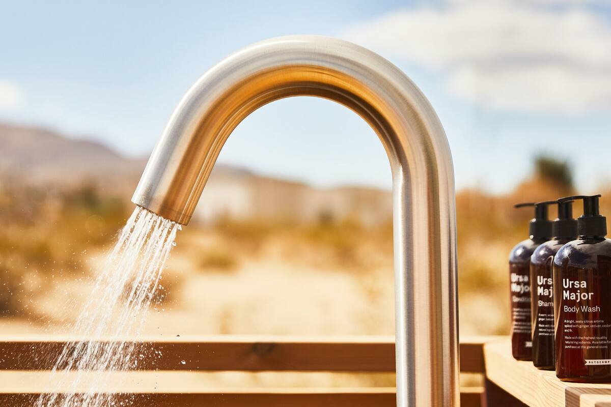 A metal faucet with water flowing into a wooden basin, with bottles of Ursa Major Body Wash on a wooden ledge.