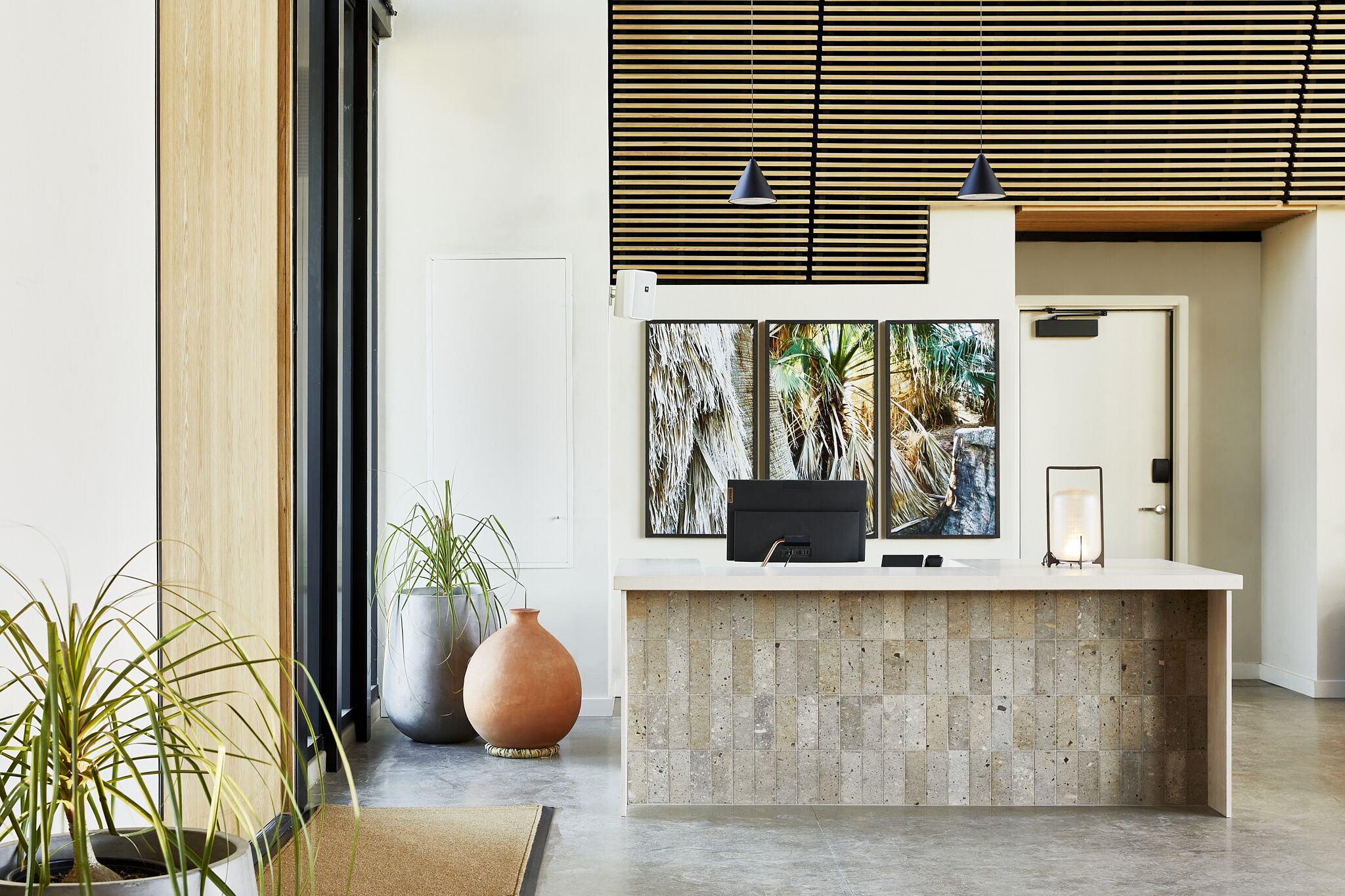 A reception desk with a tiled counter, a large framed artwork, and a potted plant.