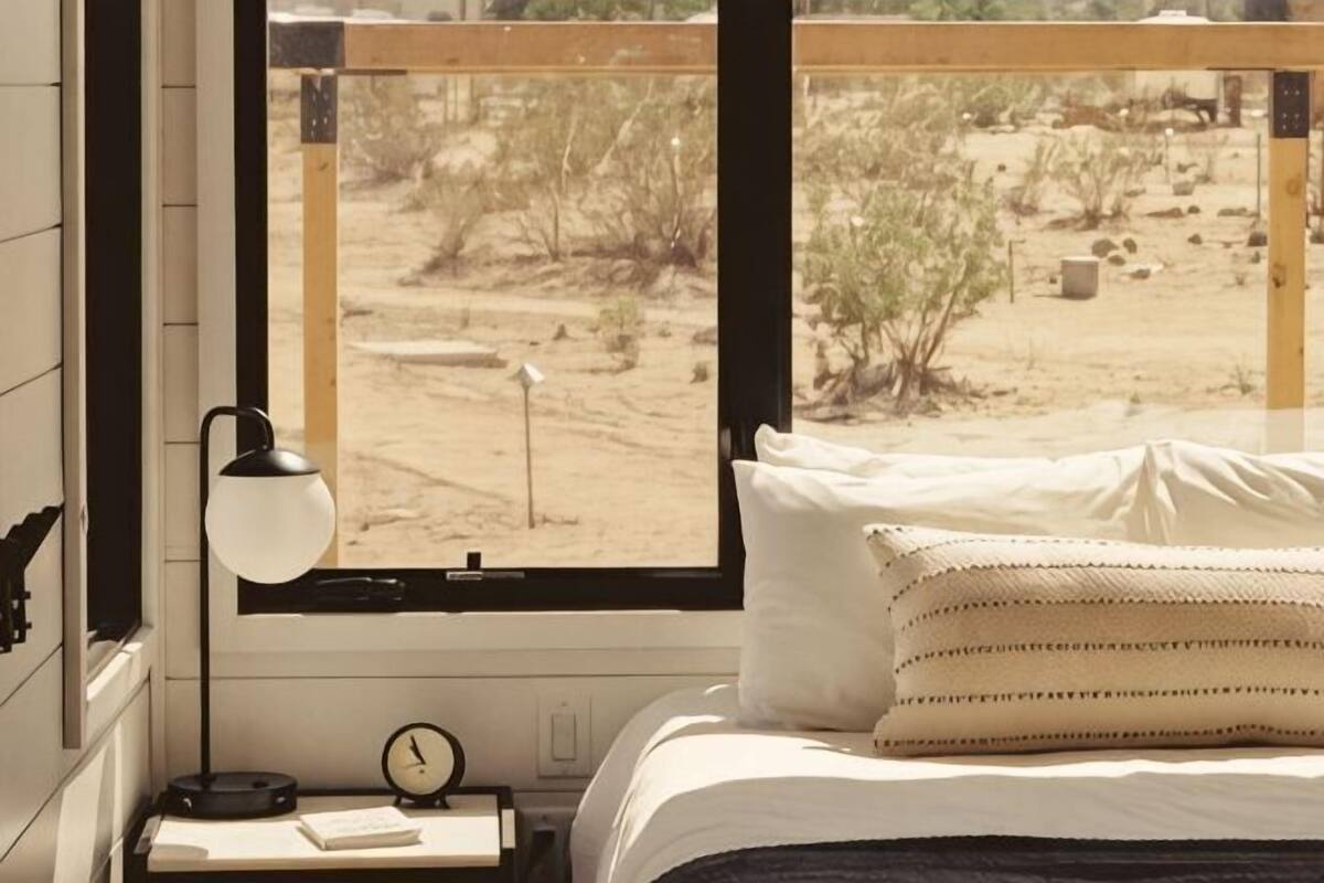 A bedroom with a bed, a bedside lamp, a clock, and a window with a desert view.
