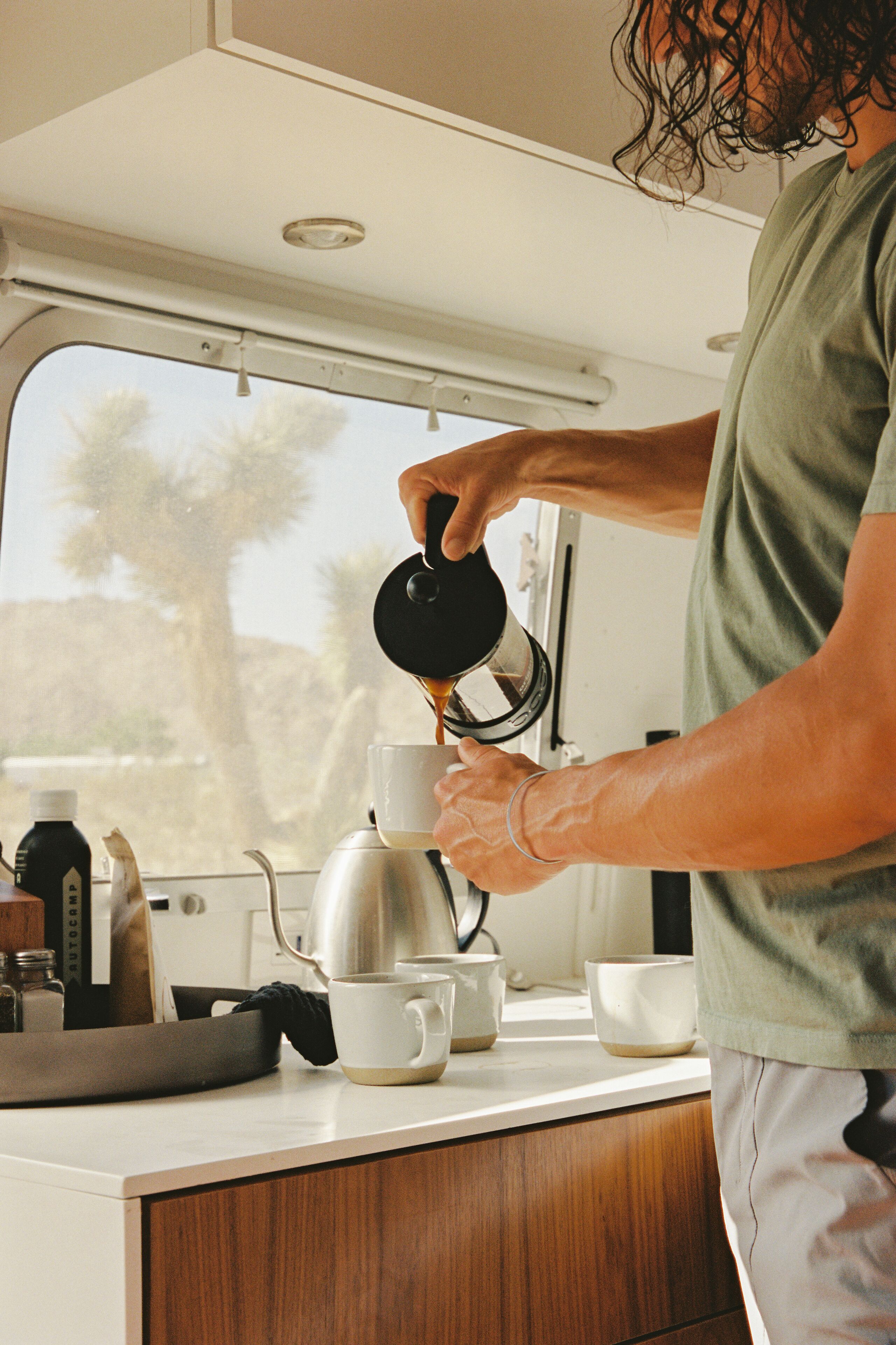 A person pouring coffee into a cup in a kitchen with a window view.