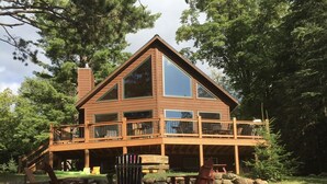 A two-story log cabin with a balcony, surrounded by trees and a grassy yard.