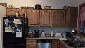 A kitchen with wooden cabinets, a black refrigerator, a dishwasher, and various kitchen appliances.