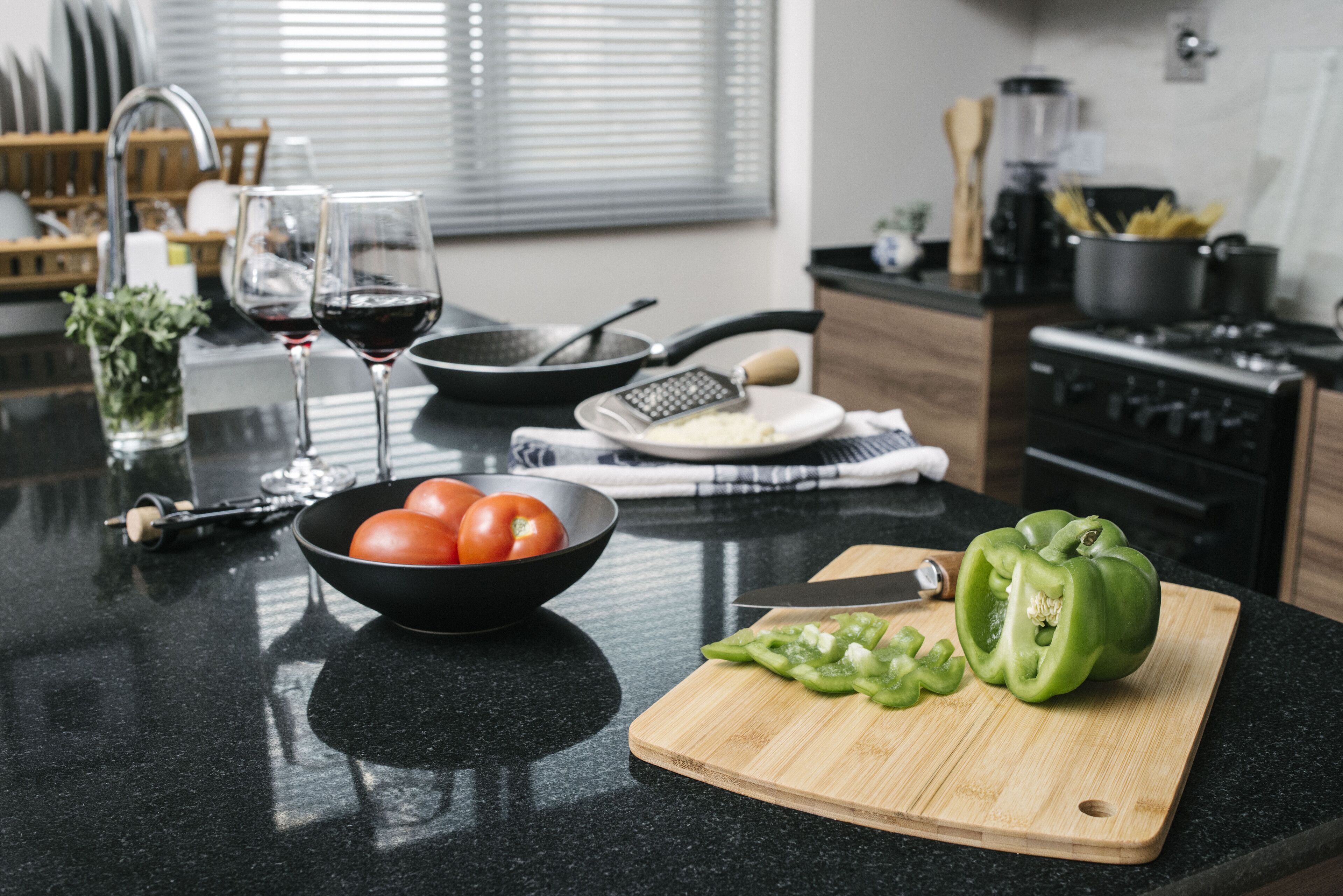 Un plan de travail de cuisine avec une planche à découper, un saladier de tomates, une râpe et un poivron vert.