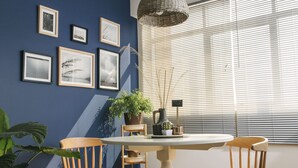 A dining area with a round table, two wooden chairs, a hanging light fixture, and framed pictures on the wall.