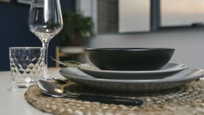 A dining setup with a glass, bowl, and spoon on a woven placemat.