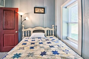 Ein Schlafzimmer mit Holztür, Nachttischlampe, Bett mit einem quiltartigen Bettbezug mit Sternenmuster, Wandschild und Fenster mit Jalousien.