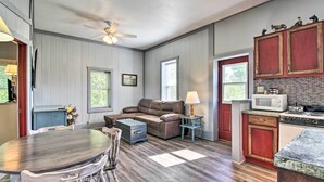 A spacious living room with a brown leather sofa, a dining table with chairs, a kitchen area with wooden cabinets and a microwave, and a ceiling fan. - Bungo Creek Retreat w/ Multi-Use Trails & a Creek (Pine River)