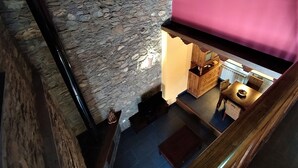 Een kamer met stenen muren, een houten trap, een klein tafeltje met een stoel en een roze muur.
