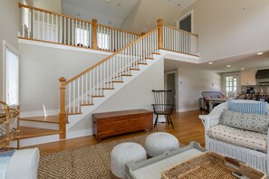 A spacious living area with a wooden staircase, a dining area, and a kitchen. - Pond View Cottage- Luxury home near Miacomet beach (Nantucket)