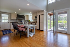 A spacious kitchen with white cabinets, a dining table with chairs, a stove, and a refrigerator. - Pond View Cottage- Luxury home near Miacomet beach (Nantucket)